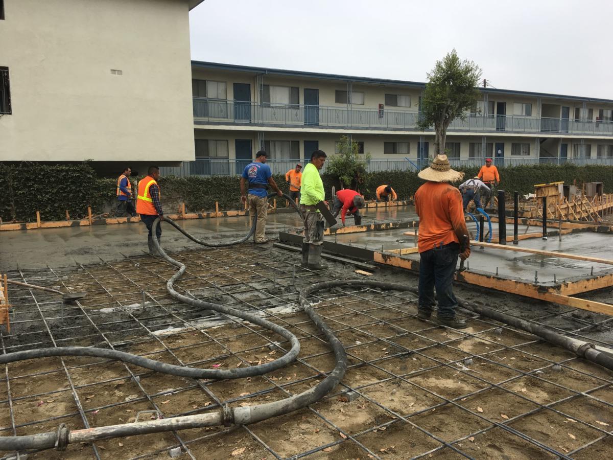 Crew placing a concrete slab with a pump truck and hose, finishers working a fresh pour